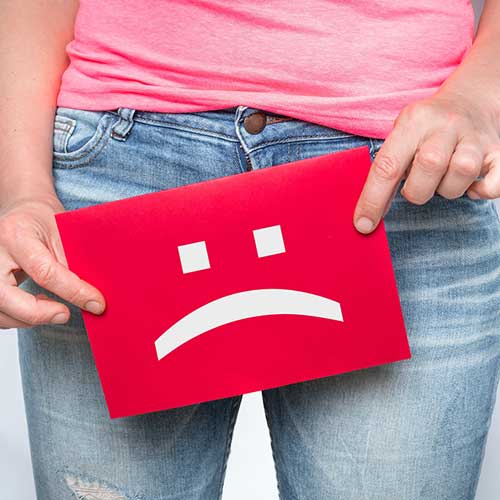 female holding sign with frowning face at waist line, indicating urinary incontinence